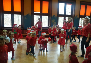 dzieci tańczą w czerwonych strojach i czapkach mikołajkowych
